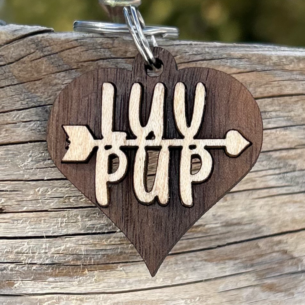 Solid walnut wood heart collar charm, with solid maple wood inlay with text  that says LUV on top of the text PUP and an arrow going between the two words. This Love Charm is attached to a spit ring 