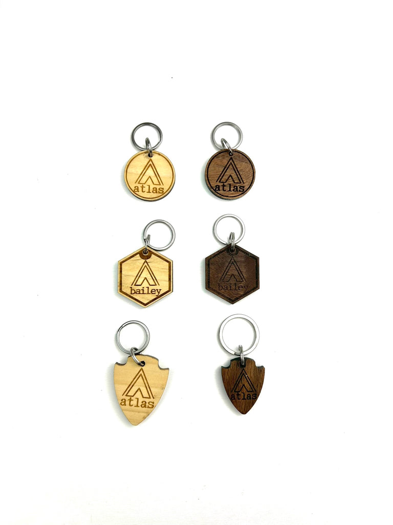 6 wooden laser engraved personalized dog ID tags (3 walnut & 3 poplar woods) with 3 different shape options ( round, hexagon, & arrowhead) with Campsite Tent background.