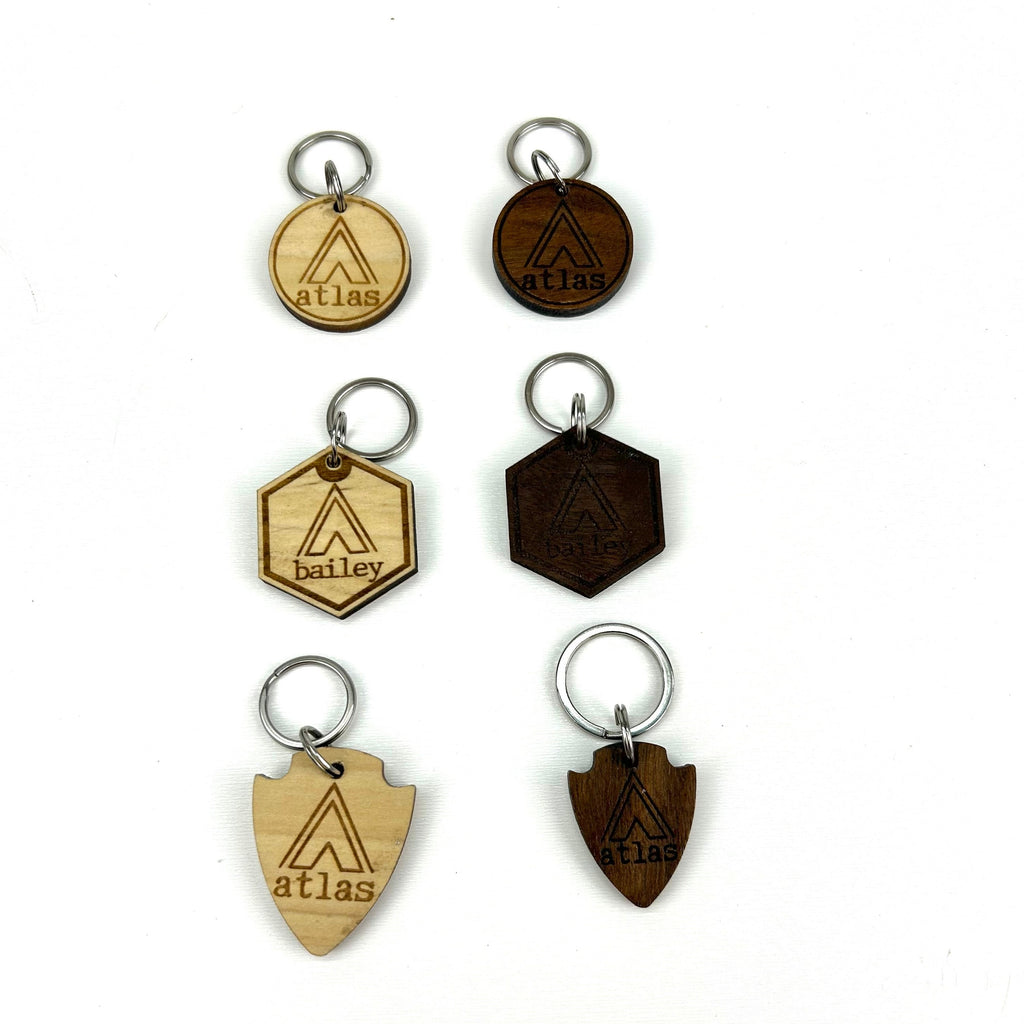 6 wooden laser engraved personalized dog ID tags (3 walnut  & 3 poplar woods) with 3 different shape options ( round, hexagon, & arrowhead) with Campsite Tent background.