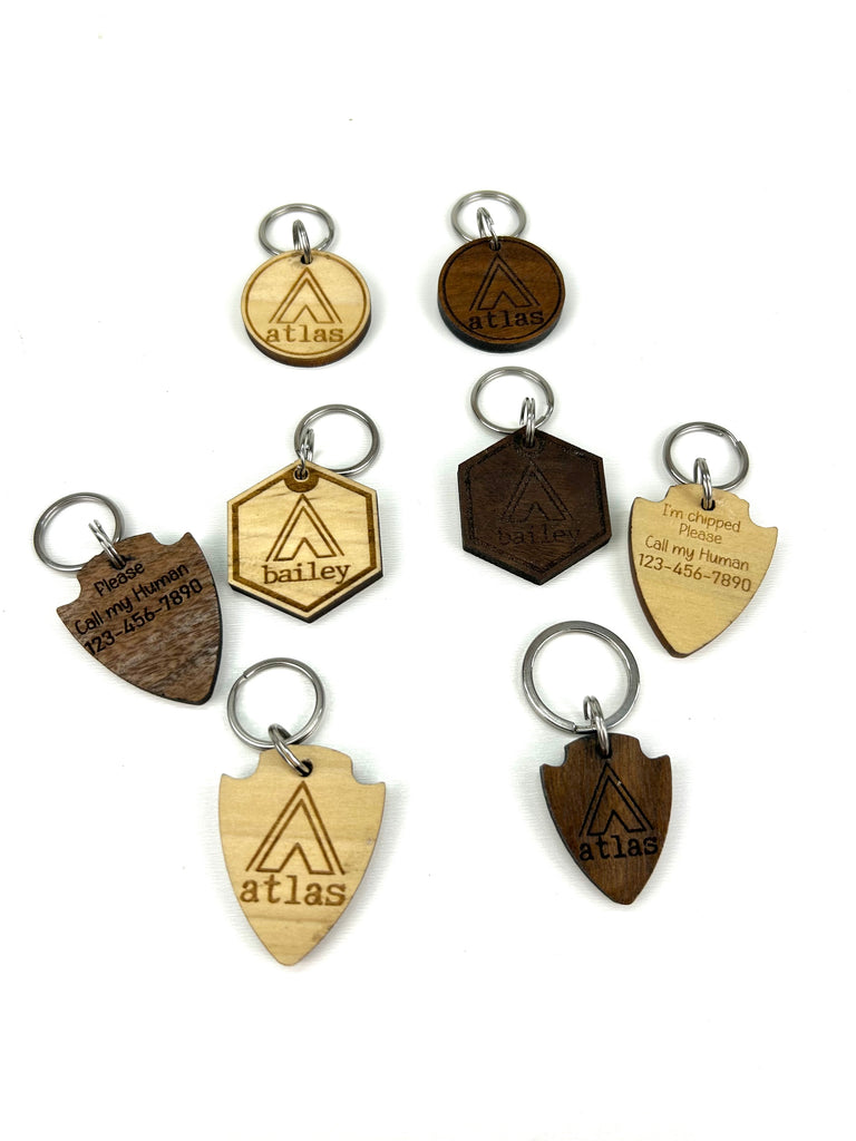 6 wooden laser engraved personalized dog ID tags (3 walnut  & 3 poplar woods) with 3 different shape options ( round, hexagon, & arrowhead) with Campsite Tent background.