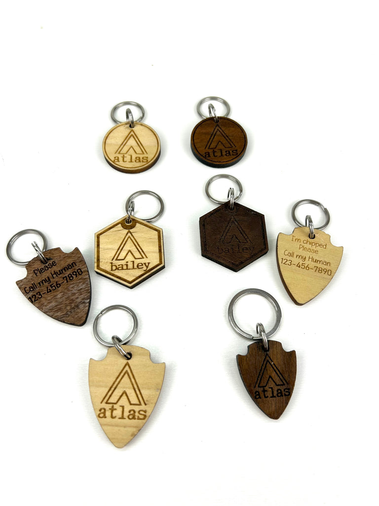 6 wooden laser engraved personalized dog ID tags (3 walnut & 3 poplar woods) with 3 different shape options ( round, hexagon, & arrowhead) with Campsite Tent background.